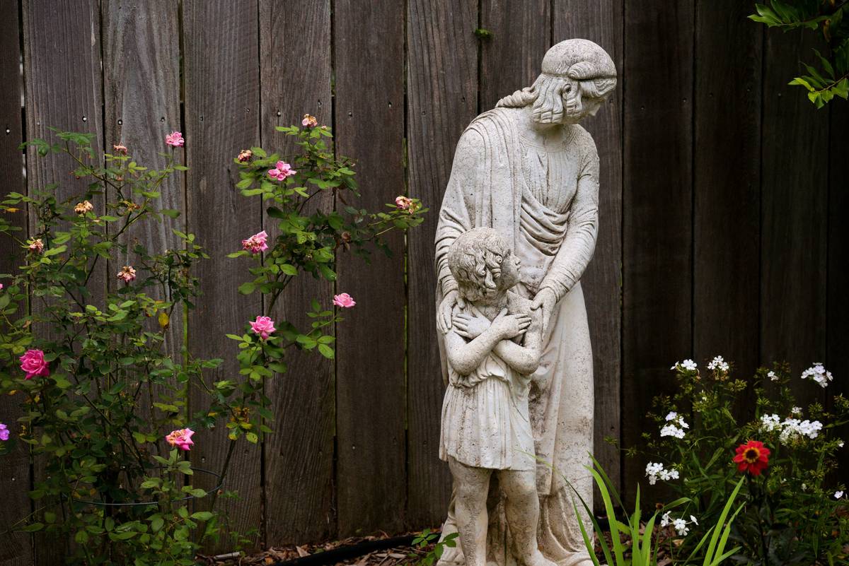 how to start an outdoor garden showing raised stone border, loamy soil, and three garden statues at varying heights on level ground
